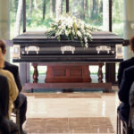 Group of people sitting at funeral, casket with flowers in front
